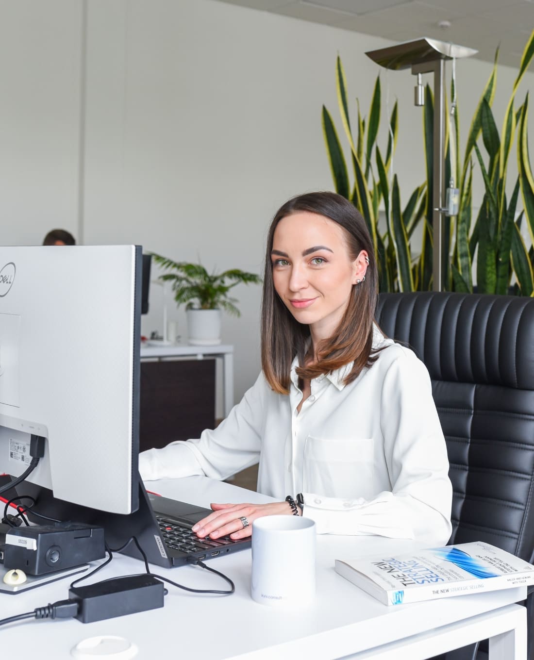 Professional research consultant at her desk using a computer, surrounded by office plants, performing market research in Europe.